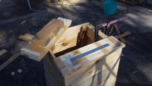 Hold or clamp the structural bit to the side of your compost bin, as shown. Wiggle you top slat around until it is in position, overhanging evenly all the way around the edge at whatever distance you chose. When you are happy, put scews through the slats into the 'beams'. Do this for all four corners.